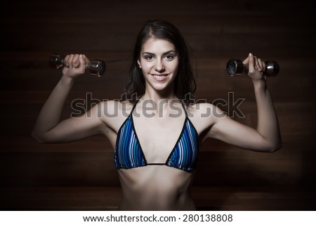 Fitness, sport, power lifting and people concept-sporty woman exercising.Low key fitness woman working out with dumbbells.Young adult fitness woman doing exercises fitness workout.Power and strength