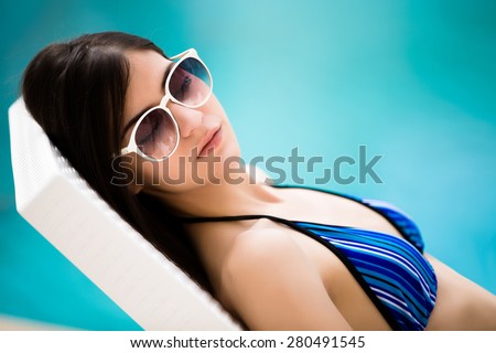 Woman enjoying in after procedures.Sexy beautiful brunette woman with in bikini relaxing beside a swimming pool in summer on tropic island.Woman relaxing in deck chair.Sunscreen,protection,summer body