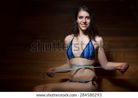 Attractive girl in bikini with tape-measure at the gym.Slim fit woman at the gym in bikini with measure tape.Woman measure waist, perfect slim body figure, female measuring tape size of belly.