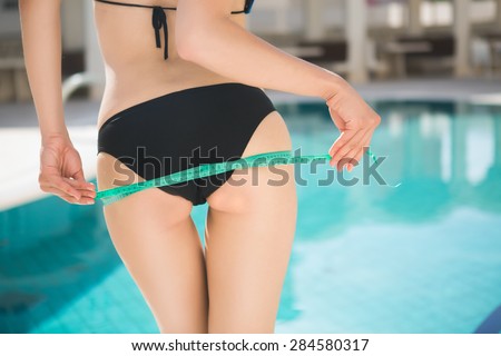 Attractive girl in bikini with tape-measure at the sea side.Slim fit woman at the pool in bikini with measure tape.woman measure hips, perfect slim body figure, female measuring tape size of hips.
