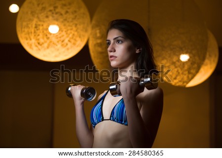 Fitness, sport, power lifting sporty woman exercising.Low key fitness woman working out with dumbbells.Young adult fitness woman doing exercises fitness workout.Power and strength