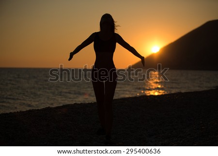 Carefree woman dancing in the sunset on the beach.Vacation vitality healthy living concept.Free woman enjoying sunset.Woman in embracing the golden sunshine of sunset,enjoying peace,serenity in nature