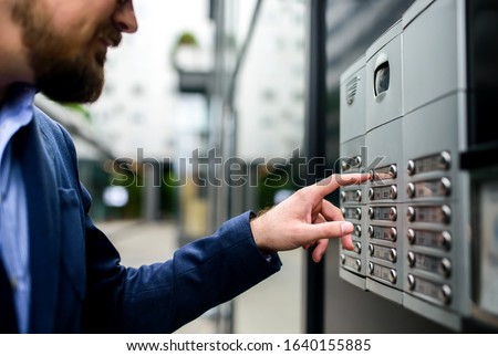 Man pushing the button and talking on the intercom in front of the apartment
