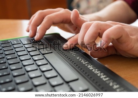 A blind man uses a computer with a Braille display and a computer keyboard. Inclusive device. Foto stock © 