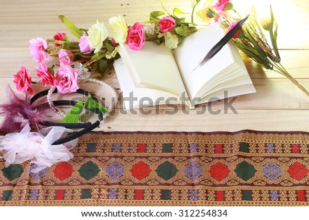 Blank old notebook, feather and flower arranged on wood table in low key