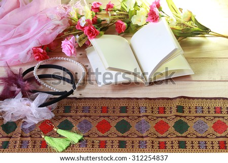 Blank old notebook, feather and flower arranged on wood table in low key