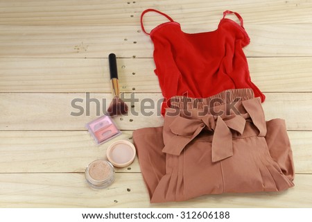 Red T-shirt and brown short woman cloth together with cosmetics on wood floor
