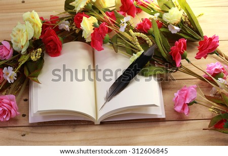 Blank old notebook, feather and flower arranged on wood table as vintage still life