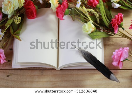 Blank old notebook, feather and flower arranged on wood table as vintage still life