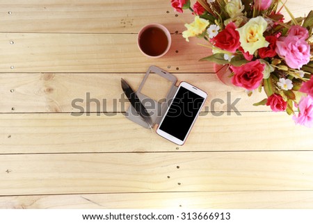smart phone and feather pen with tea cup near rose bouquet on wood table