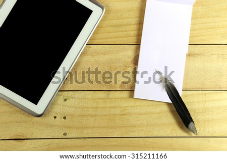 Smart phone and memo with feather pen on wood table as top view