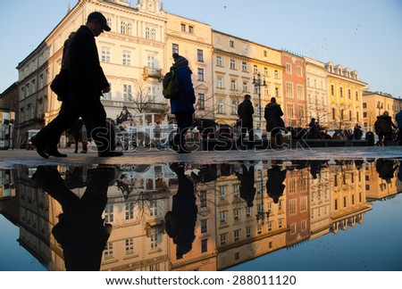 Poland, Krakow, - February 12 2015: People and buildings are reflecting in the water as they pass by central square in Krakow\'s old town.