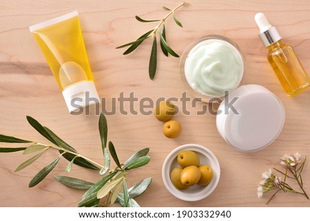 Serum and moisturizing cosmetic cream with olive extract for skin with branch and olives on wood table. Top view.