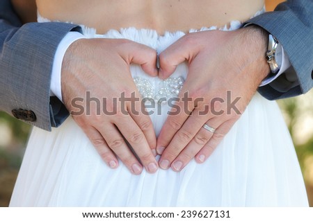 Groom making a heart with hands bride back outside