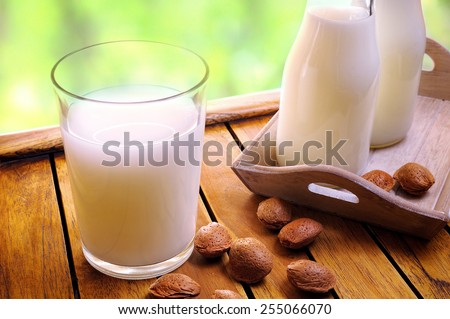 Glass of almond milk on a table with almonds and milk bottles