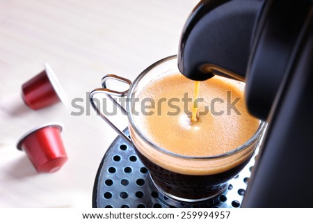 machine serving espresso coffee in a glass cup and two capsules on the table