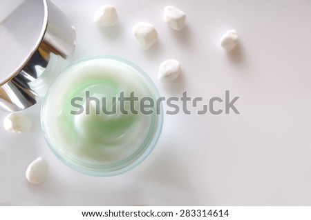 Glass open jar with facial or body cream on white table with small white stones. Top view. White isolated.