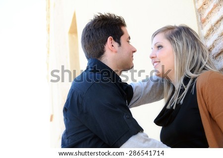Young couple in love dressed in black and brown flirting against a brick wall in a park bottom view