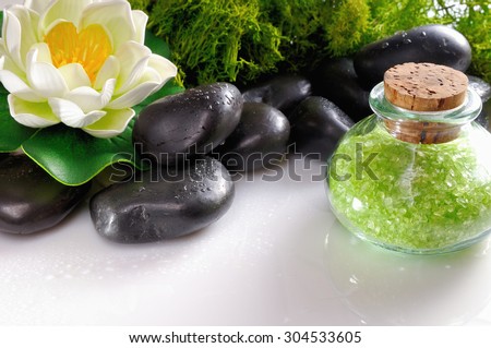 Bath salts close up with black stones and moss flower glass on white table. Horizontal composition