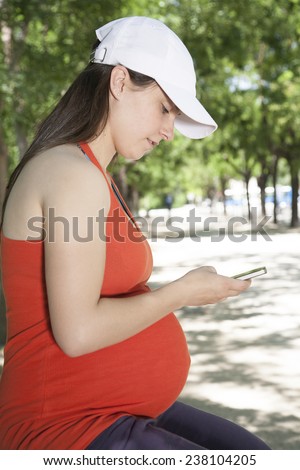 pregnant young woman with red shirt touching smartphone at a street in Madrid Spain Europe