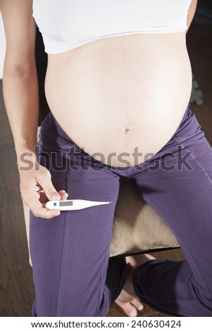 pregnant woman purple trousers bare belly sit showing in her hand blank screen smartphone