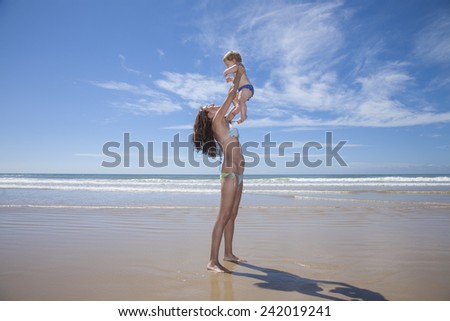 one year baby swimsuit fly in bikini woman mother arms at beach next to Conil Cadiz Spain