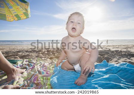 one year baby white diaper sit looking at camera backlighting over cyan towel at beach next to Conil Cadiz Spain
