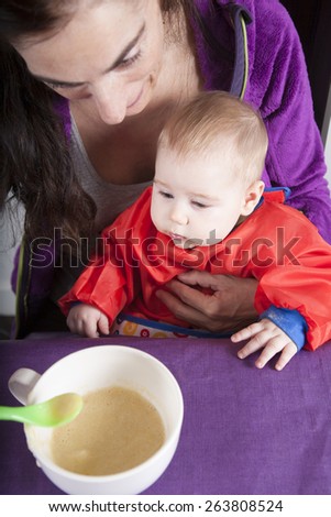 six months age blonde caucasian baby red bib in woman mother purple velvet jacket arms eating puree