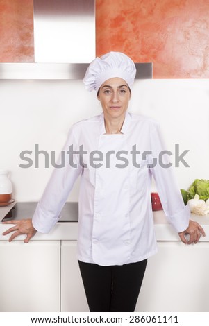 portrait of brunette chef woman with professional jacket and hat black trousers in white and orange kitchen