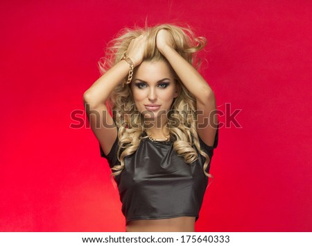 Sexy beautiful blonde woman posing in fashionable clothes, studio shot. Girl looking at camera. Red background.