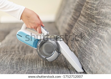 A woman vacuuming furniture in a house with a hand-held portable vacuum cleaner.