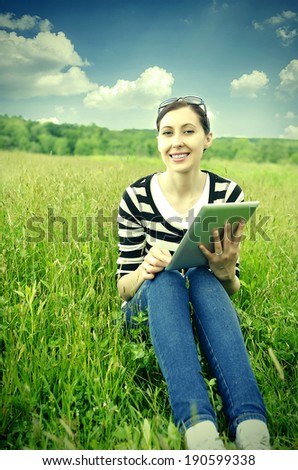 Girl with tablet computer sitting on the grass. Vintage photo.