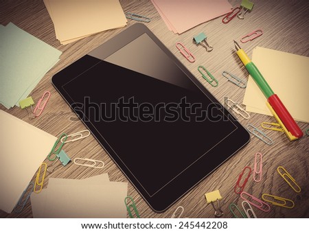 Tablet PC on the office table surrounded by multi colored paper clips. Vintage image.