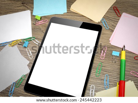 Tablet PC on the office table surrounded by multi colored paper clips and notebooks