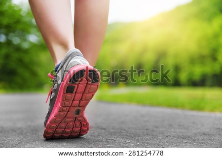 Woman\'s legs in shoes on runner jogging in the park at sunset.