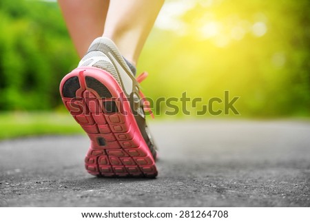 Woman\'s legs in shoes on runner jogging in the park at sunset.