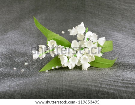 lilies of the valley of artificial white satin fabric with green leaves on pearl gray background with the flickering light