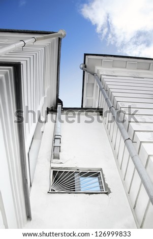 window on the wall of the city house of gray stone color with a tin trumpet and metal bars on the window from the perspective of the past in the sky on the background of a bright blue sky and clouds