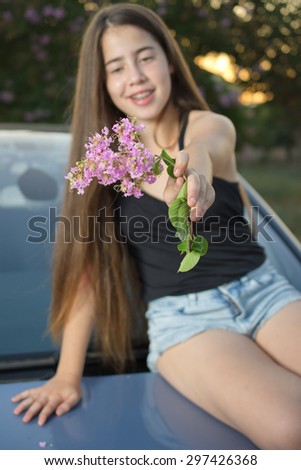 A 13 year old teenage girl with braces on her teeth sitting on a car enjoying pink flowers and the summer sunset (focus on the flowers)