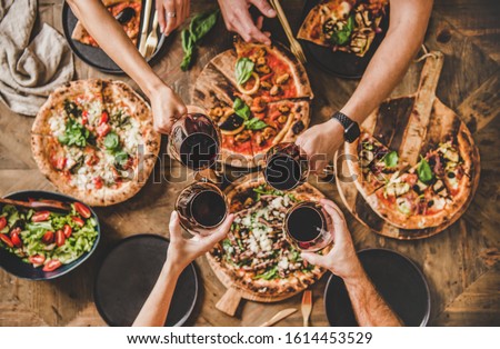 Family or friends having pizza party dinner. Flat-lay of people clinking glasses with red wine over rustic wooden table with various kinds of Italian pizza, top view. Fast food lunch, celebration