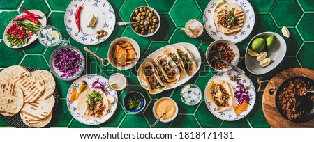 Family or friends home taco party. Flat-lay of Mexican traditional dishes Tacos with beef meat, corn tortillas and tomato salsa over green tile table background, top view. Mexican cuisine concept