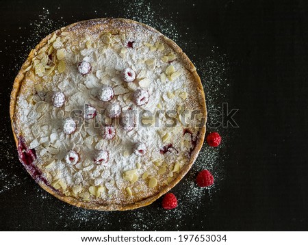 A pie with fresh raspberries, almond and sugar powder on a black background