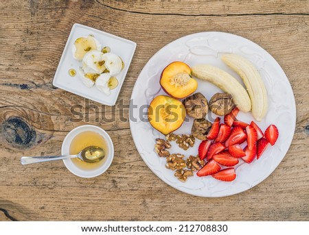 Breakfast set with fresh strawberry, banana, peach, dry figs, walnuts, soft goat cheese and honey on a rough wooden surface