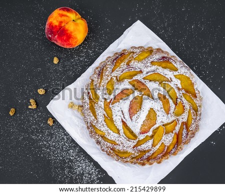 Peach pie with sugar powder over a piece of paper on a dark surface