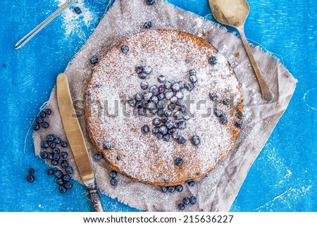 Blueberry cake with fresh blueberries, sugar powder, a knife and a blade over a blue painted wooden surface