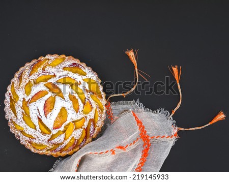 Peach pie with sugar powder over a linen table cloth on a dark surface