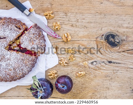 Plum cake with walnuts and fresh ripe plums on white paper over a rough wood background