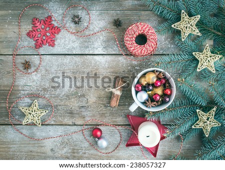 Christmas (New Year) decoration background with a copy space: a cup of colorful Christmas tree toys, cinnamon sticks, toy stars, a candle and a decoration rope on a rustic wooden desk. Top view