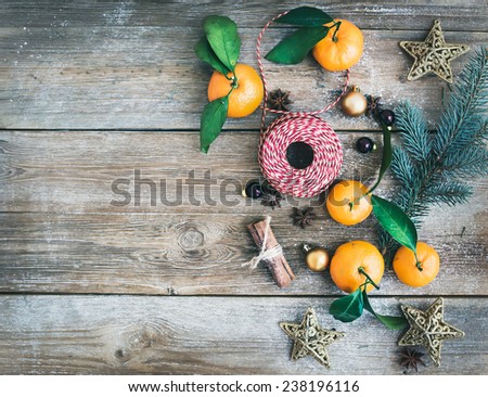 Christmas (New Year) decoration background set: fur-tree branches, glass balls, golden glittering toy stars and mandarines with green leaves on a rough wooden desk with a copy space. Top view