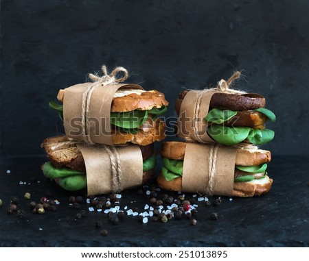 Cured chicken and spinach whole grain sandwiches placed one on another wrapped in craft paper and tied with a decoration rope  with spices and black stone background